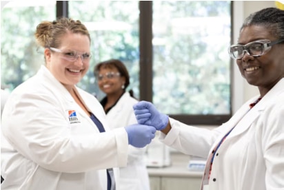 three smiling women, scientists in white coats and protective glasses