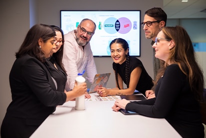 A team working together. In the background, an interactive board with the Palmolive and Ajax logos